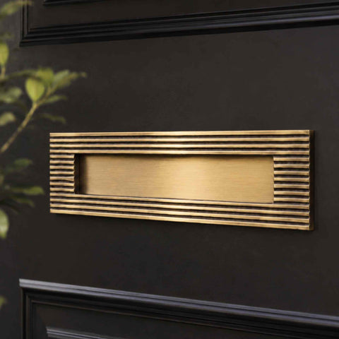 Antique brass reeded letter box plate installed on a black front door