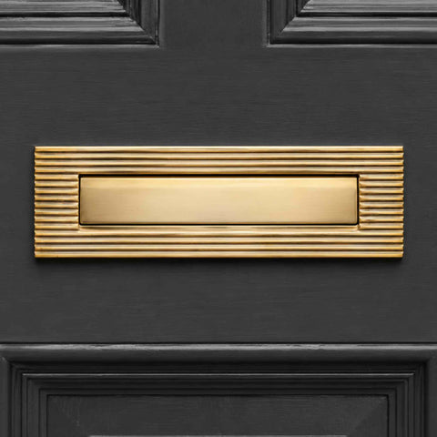 Close-up of polished brass reeded letter box plate with sprung flap on a black entrance door