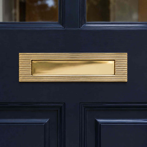 Polished brass reeded letter box plate fitted to a traditional black front door