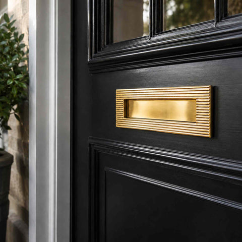 Angled lifestyle view of polished brass reeded letter box plate on a black entrance door