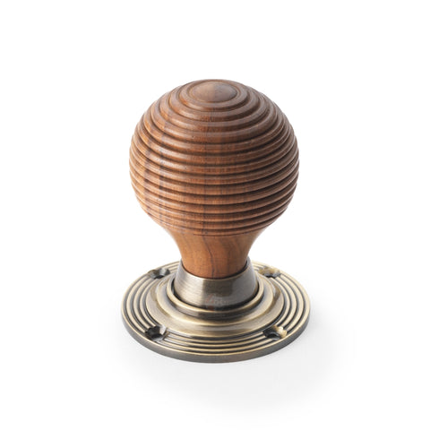 Single rosewood beehive door knob with antique brass reeded backplate on white background