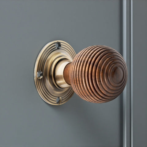Rosewood beehive antique brass door knob installed on grey panel door front angle view