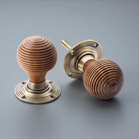 Pair of rosewood beehive door knobs with antique brass backplates on grey background