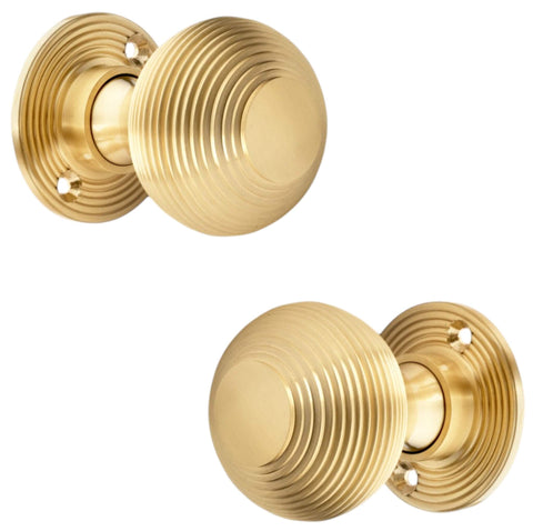 Pair of satin brass reeded mortice door knobs shown from side profile angle on white background