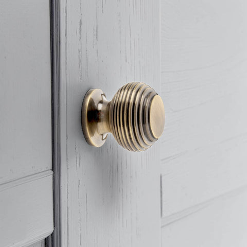 Small antique brass beehive cupboard knob fitted on cabinet door, traditional reeded brass drawer knob close up