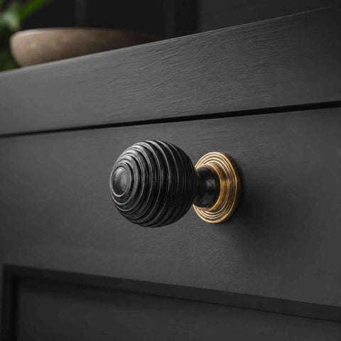 Small ebonised black beehive cupboard knob with unlacquered aged brass backplate fitted to a dark painted drawer.