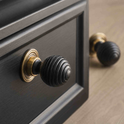 Ebonised beehive cupboard knobs with unlacquered aged brass backplates fitted to dark painted furniture drawers.