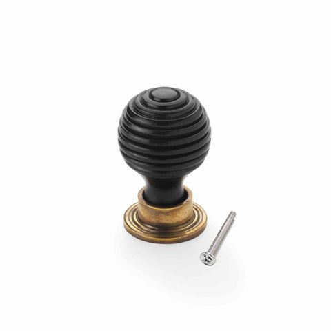 Small ebonised beehive cupboard knob with unlacquered aged brass backplate and fixing bolt on a white background.