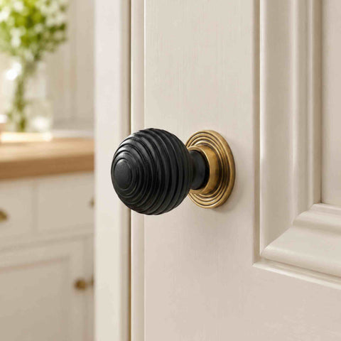 Small ebonised black beehive cupboard knob with aged brass backplate fitted to a cream painted cabinet door.