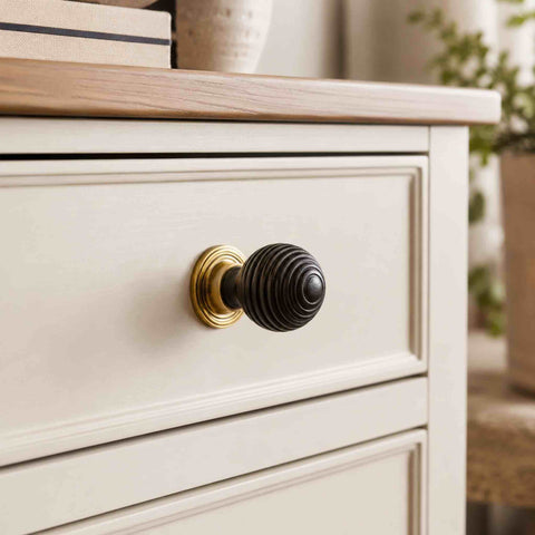 Small ebonised black beehive cupboard knob with aged brass backplate fitted to a cream painted chest of drawers.