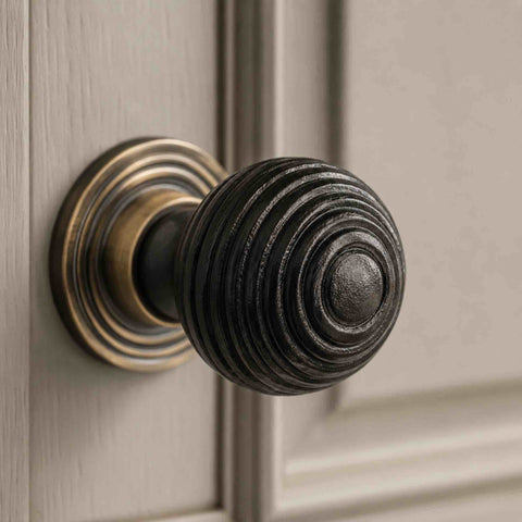 Close-up of small ebonised black beehive cupboard knob with antique brass backplate fitted to a light painted cabinet door.