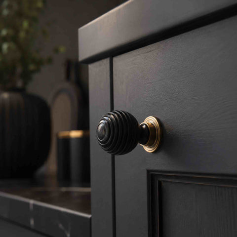 Small ebonised beehive cupboard knob with antique brass backplate fitted to a dark painted cabinet in a traditional interior.