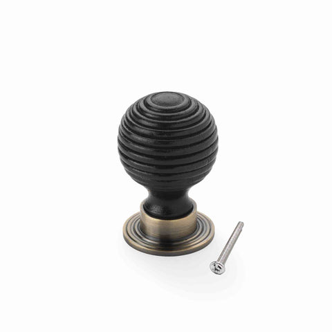 Small ebonised black beehive cupboard knob with antique brass backplate and fixing bolt displayed on a white background.