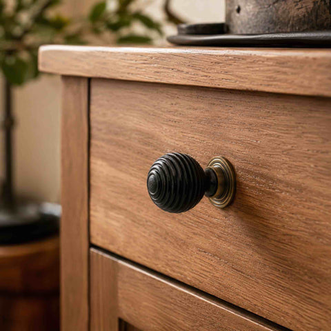Ebonised beehive cupboard knob with antique brass backplate fitted to a natural wooden chest of drawers.