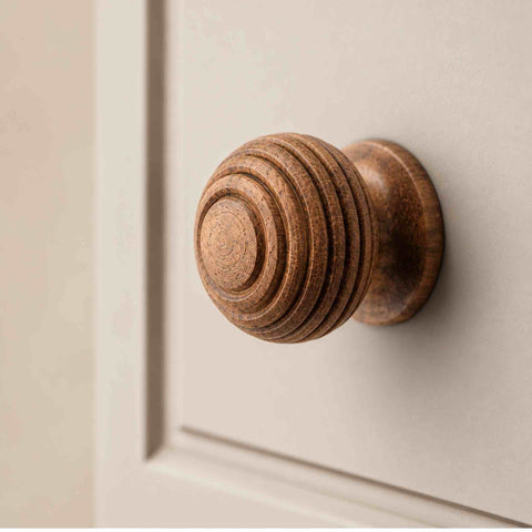 Close-up of a small rosewood beehive cupboard knob fitted to a cream painted cabinet door.