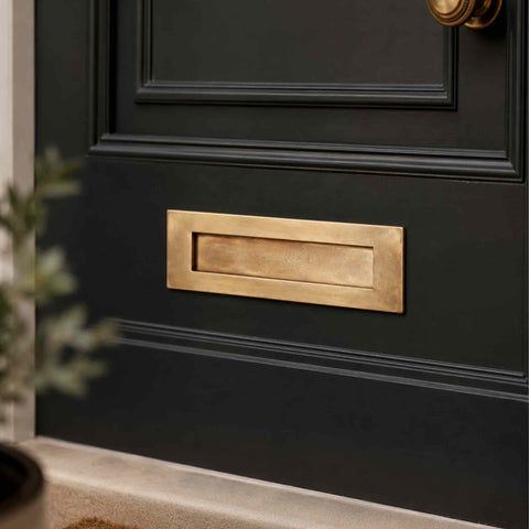 Aged brass letter plate fitted to a dark front door, showcasing the warm aged finish, recessed flap design and premium entrance styling.
