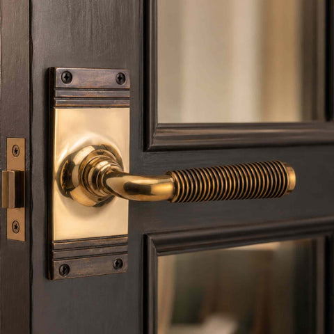 Close-up of a solid aged brass reeded lever handle on a matching backplate, highlighting the detailed reeded texture and aged brass finish.