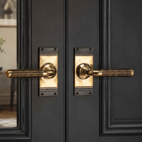 Pair of solid aged brass reeded lever door handles fitted to black double doors, creating a striking traditional entrance feature.