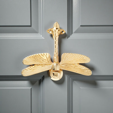 Solid brass dragonfly door knocker with an unlacquered polished brass finish fitted to a grey front door.