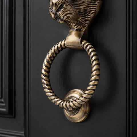 Front view of antique brass hare door knocker installed on a black panelled entrance door