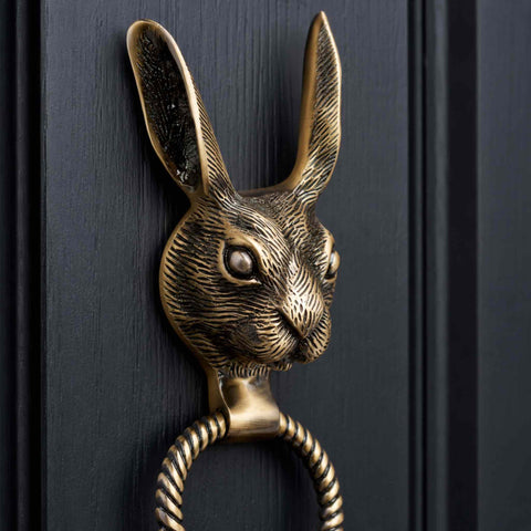 Close-up of antique brass hare door knocker highlighting the twisted reeded ring and strike plate