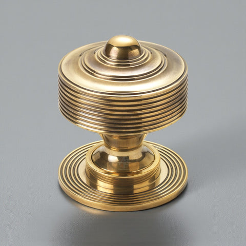 Solid brass reeded centre door knob in unlacquered aged brass finish shown against a grey background.