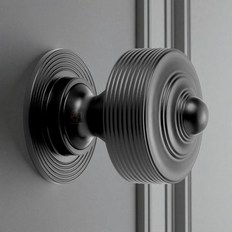 Powder coated black reeded centre door knob installed on a door, highlighting its ridged detailing and round base.