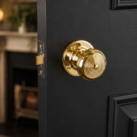 Unlacquered Polished Brass Ringed Christoph Mortice Door Knob fitted to a black panelled door with polished brass latch