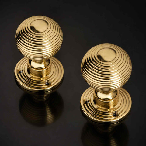 Pair of polished brass beehive door knobs with matching reeded backplates displayed on a black background